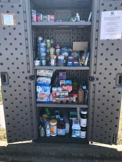A tan cabinet with doors open to show it is full of canned goods and other nonperishable food